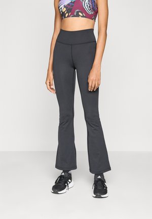 Pantaloni atletici negri evazați, cu o textură netedă și elastică, asortați cu un top scurt cu imprimeu colorat de fluturi și adidași negri.