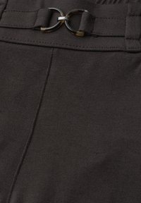 Gros plan sur un pantalon en tissu foncé montrant une boucle de ceinture double anneau en écaille de tortue et des passants à la taille.
