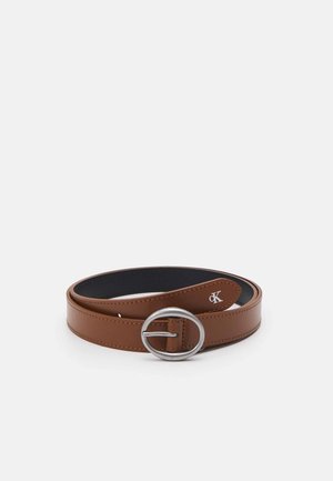 Brązowy skórzany pasek z owalną srebrną klamrą i małym białym logo "CK" wytłoczonym blisko końca klamry, ułożony płasko na białym tle.