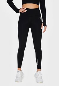 Czarne legginsy z wysokim stanem wykonane z elastycznego materiału o gładkiej fakturze. Posiadają białe logo "SQUATPROOF" przy kostce.