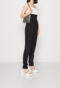 Zwarte jumpsuit met een vierkante halslijn en een witte top. Gecombineerd met witte plateauzandalen en een zilverkleurige handtas met textuur.