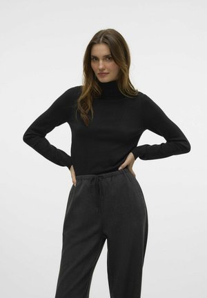 Pull à col roulé noir à manches longues, fabriqué en tissu lisse. Associé à un pantalon gris foncé, ample, avec taille à cordon.