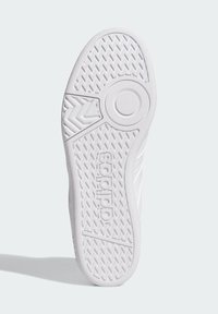 Hvid sneakersål med teksturerede grebmønstre, der har et cirkulært accent og det fremtrædende "adidas"-logo.