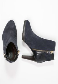 Stivaletti alla caviglia in suede blu navy con punta affusolata, dettagli in pelle nera e zip laterale. Caratterizzati da un tacco impilato testurizzato.
