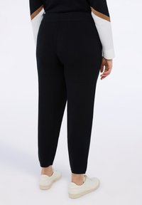Czarne spodnie o gładkiej fakturze i zwężanym kroju, z elastycznym pasem. W połączeniu z białymi trampkami.