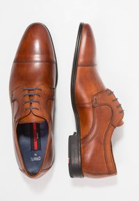 Une paire de chaussures de ville en cuir marron poli avec des semelles noires, une chaussure vue de dessus et l'autre de côté.