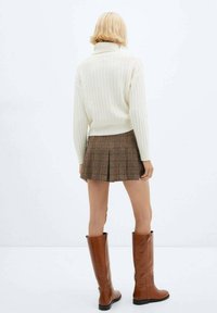 Crème ribbel turtlenecktrui gecombineerd met een geruite mini-jurk en bruine leren kniehoge laarzen, die een gestructureerde uitstraling laat zien.