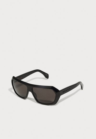 Black oversized sunglasses with an angular design, dark tinted lenses, and sleek black temple arms featuring small holes for ventilation.
