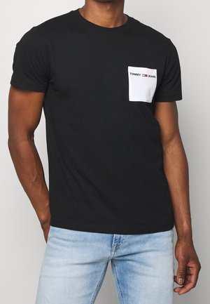 Black cotton t-shirt featuring a white chest pocket with "TOMMY JEANS" logo in red. Short sleeves and crew neck design.