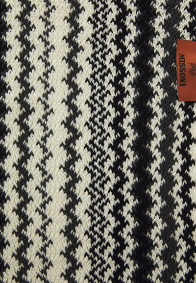 Melnas un baltas rakstainas audums ar ievītu suņu zobu dizainu un brūnu etiķeti, uz kuras baltā tekstā rakstīts "MISSONI".