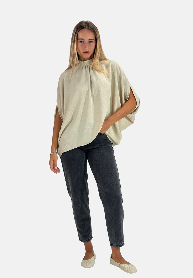 Blusa oversize beige chiaro con colletto alto, design plissettato, maniche corte, abbinata a jeans grigi scuri a gamba affusolata e scarpe slip-on color crema.