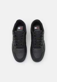 Svarta sneakers med en slät läderyttare, rund tå, svarta snören och märkesetiketter med röda, vita och blå accenter.