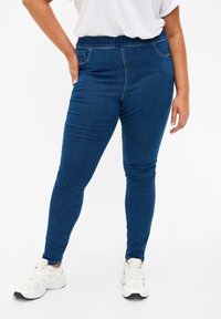 Denim leggings with a dark blue hue, featuring a stretchy elastic waistband, faux front pockets, and a slim fit. Designed for comfort.