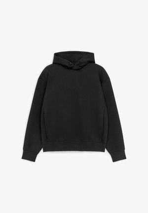 Felpa nera a maniche lunghe con cappuccio, tasche frontali, polsini a coste e coulisse regolabili sul cappuccio, disposta distesa su sfondo bianco.