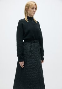 Sweatshirt preto de malha com gola alta, apresentando uma marcação subtil, combinado com uma saia longa e texturizada preta acolchoada com detalhes de cinto.