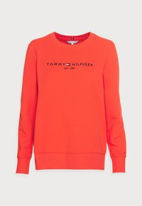 Světlý oranžový svetr vyrobený z bavlny, s kulatým výstřihem, dlouhými rukávy a logem "TOMMY HILFIGER EST. 1985" v černé barvě napříč hrudníkem.