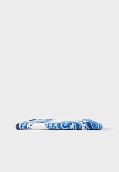 Serviette blanche pliée avec des motifs floraux et cachemire bleus complexes sur un fond clair uni.