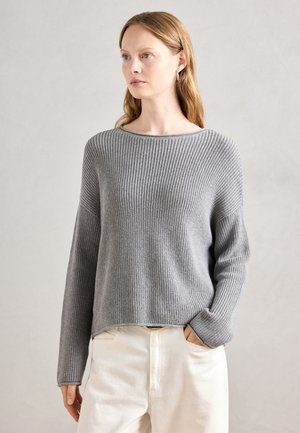 Pull en tricot gris avec un large décolleté et une coupe décontractée. Manches longues et ourlet légèrement court. Porté sur un pantalon de couleur claire.
