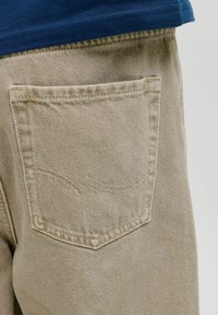Pantalones de mezclilla beige con un bolsillo trasero con detalles de costura curvada. La tela tiene una textura sutil y un diseño de corte clásico.