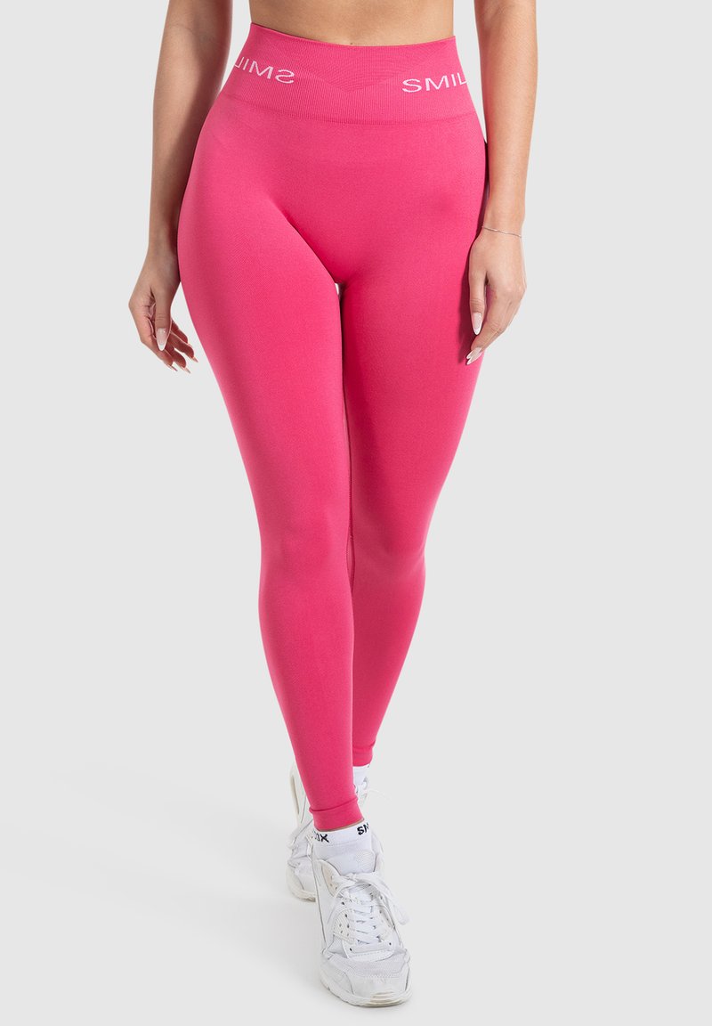 Leggings rosa con un alto cinturino che mostrano il testo "SMIL". Il tessuto è liscio con un design aderente e elastico, perfetto per l'abbigliamento sportivo.