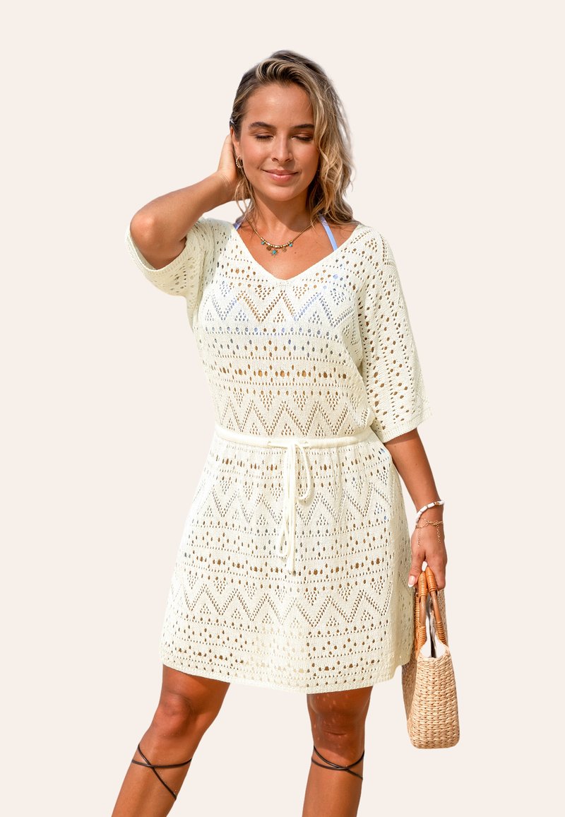 Lichte crème haakjurk met een V-hals, korte mouwen en zigzagpatroon. Heeft een trekkoord in de taille en een ontspannen pasvorm.