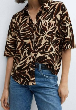 Personne portant une chemise à manches courtes boutonnée avec des motifs abstraits de feuilles marron foncé et beige, rentrée dans un jean bleu avec une ceinture noire.