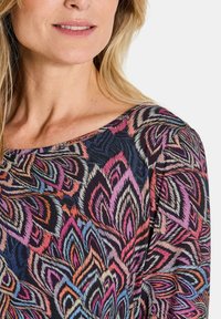 Gestreepte top met een ronde hals. Het ontwerp bevat levendige bloemenmotieven in roze, blauw en zwart, met een zachte textuur.