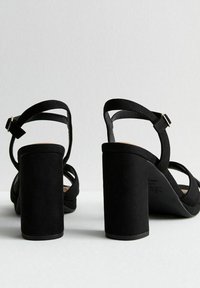 Sandalias de tacón bloque de ante negro con correas ajustables en el tobillo y punta abierta. Presentan una textura suave y un diseño minimalista.