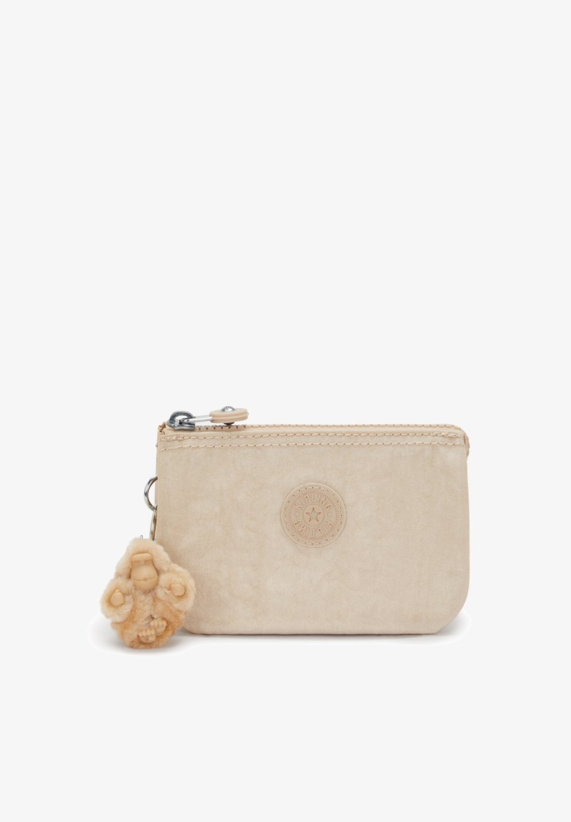 Beżowa saszetka wykonana z miękkiego materiału, z teksturowaną powierzchnią i okrągłym logo. Zawiera pluszowego małpkę na breloczku przymocowaną metalowym klipsem.