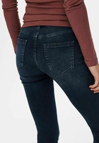 Jeans bleu foncé à coupe slim, avec deux poches arrière et un tissu en denim légèrement texturé et lisse. La taille est mi-haute.
