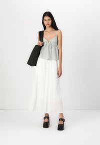 Crop top à carreaux gris et blancs avec un nœud à l'avant, associé à une longue jupe blanche fluide et des talons plateformes noirs épais.