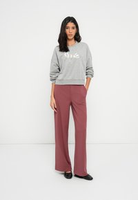 Gray oversized sweatshirt with "Smile" in sequins, paired with wide-leg maroon pants. Model wears black flats, demonstrating casual attire.