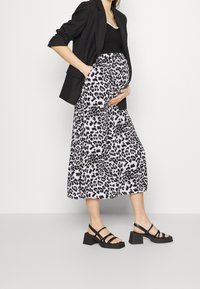 Svart blazer över en svart topp, matchat med en kjol i medellängd med ett vitt och svart leopardmönster. Svarta remsandaler med blockklack.