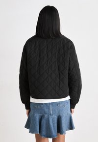 Svart quilted bomberjakke med elastiske mansjetter, kombinert med en hvit skjorte og et utsvingt denimskjørt som viser diamantmønstertekstur.