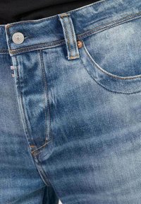 Lichtblauwe denim jeans met vervagingseffecten, voorzien van een voorkeurszak, metalen knoopsluiting en oranje stiksels.