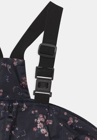 Donker gekleed met bloemenpatroon, voorzien van verstelbare zwarte banden en een ritsdetail, met een gladde, glanzende textuur.