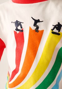 Weißes T-Shirt mit roten Ärmeln, das ein Regenbogenmotiv in Orange, Gelb und Rot mit drei schwarzen Silhouetten von Skateboardern zeigt.