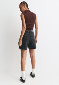 Schwarze Denim-Shorts mit fransigem Saum, kombiniert mit einem bordeauxfarbenen, anliegenden Oberteil mit Rippenstruktur. Schwarze Sneaker und weiße Socken runden das Outfit ab.