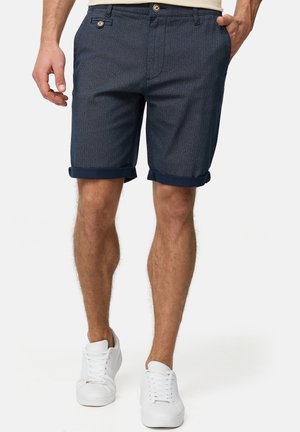 Navyblå shorts med et tekstureret mønster, opkrogede kanter og sidelommer. Færdiggjort med en knaplukning og bæltestropper, kombineret med hvide sneakers.