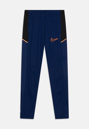 Pantalones deportivos navy con paneles laterales negros, detalles en naranja y logo de Nike en la parte inferior delantera, fabricados con un tejido ligero y transpirable.