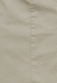 Gros plan sur un tissu beige montrant une couture verticale avec des détails de couture visibles au centre.