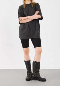 T-shirt nero oversize con maniche corte abbinato a pantaloni bike neri a coste. Il modello indossa stivali neri in pelle al ginocchio con fibbie.