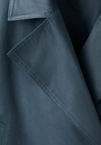 Abrigo azul oscuro con un gran cuello, textura suave y detalles de costuras visibles. La tela parece ligera y resistente.