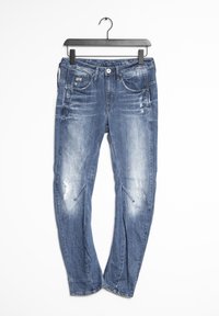 Blå denimjeans med en urtvättad finish och slitna detaljer. Inkluderar fickor och en knäppning. Hänger från en svart krok.