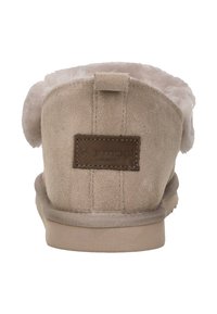 Beige suède pantoffels met een zachte, fluffy binnenkant, een gestikte zool en een bruine leren label achterop, met een lusvormige trekstrip.