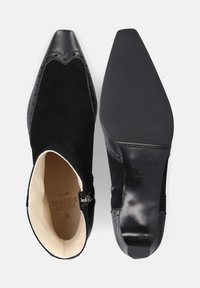 Zwarte enkelaars met een bovenkant van suède, spitse neus en golvende details. Voorzien van een zijrits en een gladde, platte zool. Maat 38.