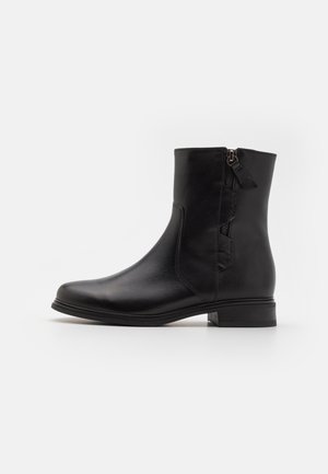 Botín de cuero negro hasta el tobillo con un acabado suave, cremallera lateral, diseño minimalista y tacón bajo cuadrado. Acolchado internamente para mayor comodidad.