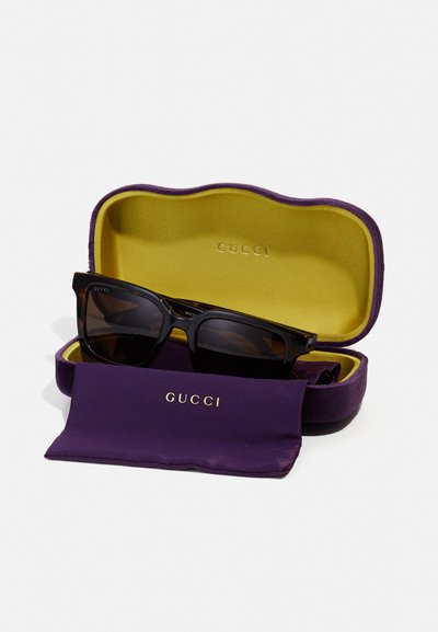 Gucci-zonnebrillen in een donker acetaat frame, tentoongesteld in een paarse en gele hardcase met een bijpassende doek voor het schoonmaken.