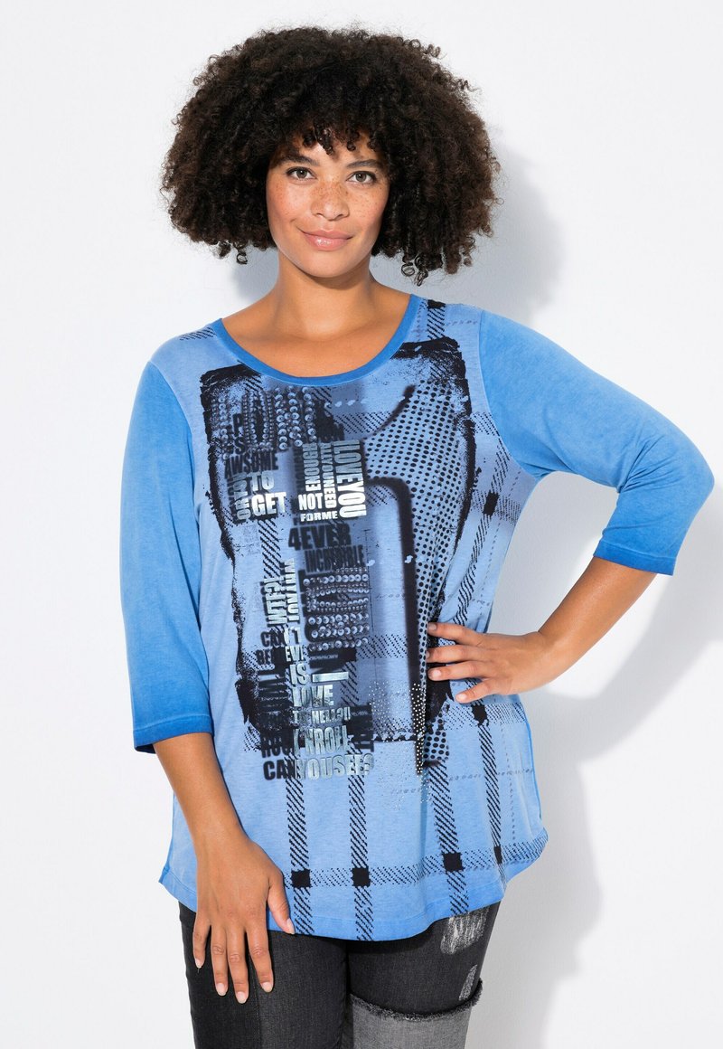 T-shirt à manches longues bleu avec du texte graphique et des motifs dans différentes nuances de bleu, présentant un col rond et une coupe décontractée.