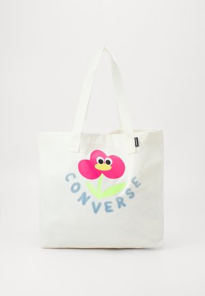 Sac cabas blanc avec longues anses, représentant une fleur rose avec des yeux et un bec jaune, une tige et des feuilles vertes, avec "CONVERSE" écrit en dessous.